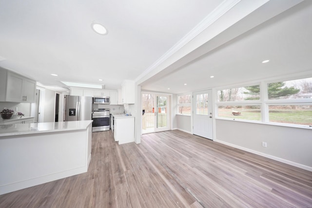 kitchen featuring open floor plan, stainless steel appliances, light countertops, and crown molding