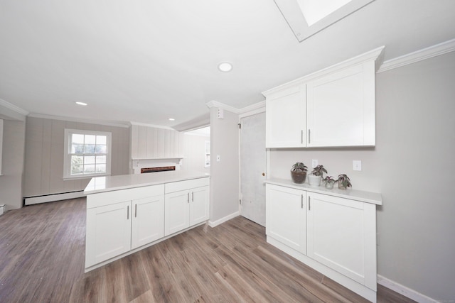 kitchen with light countertops, ornamental molding, white cabinets, wood finished floors, and a baseboard radiator