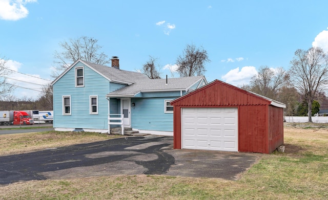 view of front of home featuring a shingled roof, an outbuilding, a chimney, and aphalt driveway