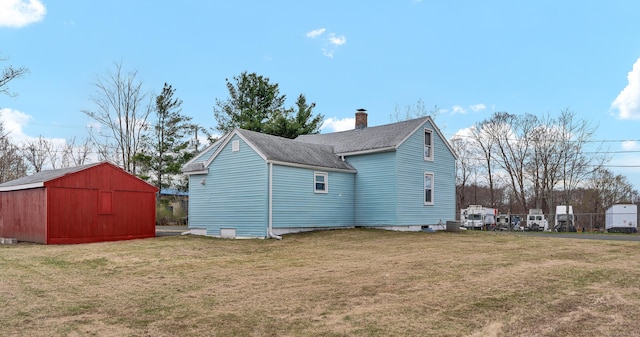 back of property with a storage shed, an outbuilding, a chimney, a yard, and roof with shingles