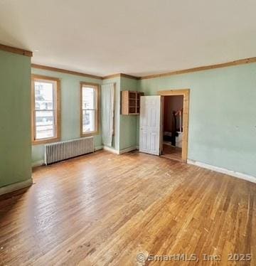 empty room with radiator heating unit, baseboards, wood finished floors, and ornamental molding