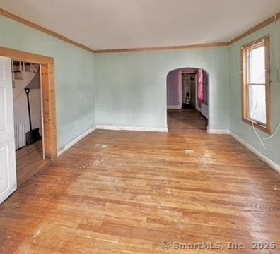 empty room with arched walkways, light wood-type flooring, baseboards, and ornamental molding