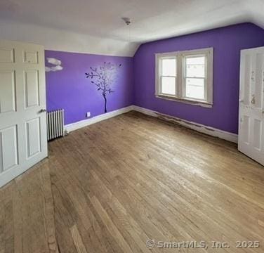 additional living space with lofted ceiling, wood finished floors, and radiator