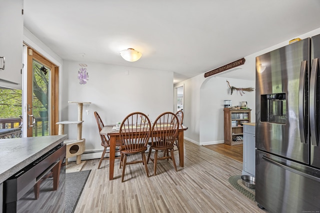 dining room featuring baseboard heating, light wood finished floors, arched walkways, and baseboards