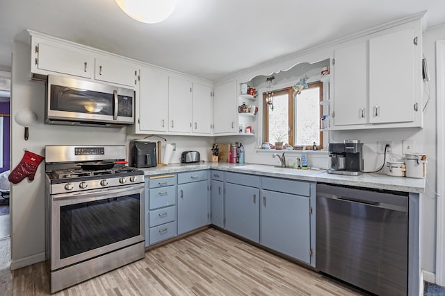 kitchen with a sink, stainless steel appliances, light wood-type flooring, white cabinetry, and light countertops