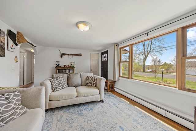 living area featuring baseboard heating, baseboards, arched walkways, and wood finished floors