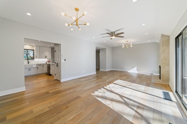 unfurnished living room with light wood-type flooring, visible vents, baseboards, and ceiling fan with notable chandelier