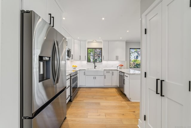 kitchen with a sink, white cabinets, light wood-type flooring, stainless steel appliances, and backsplash