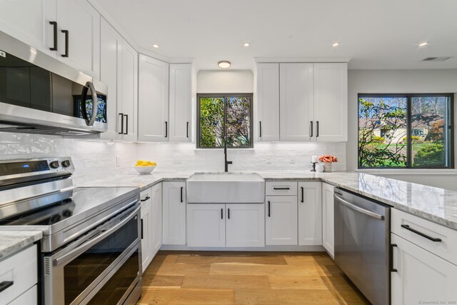 kitchen featuring stainless steel appliances, visible vents, a sink, light wood-style floors, and white cabinetry