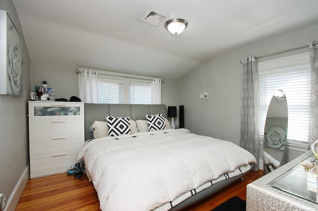 bedroom with baseboards, visible vents, wood finished floors, and vaulted ceiling