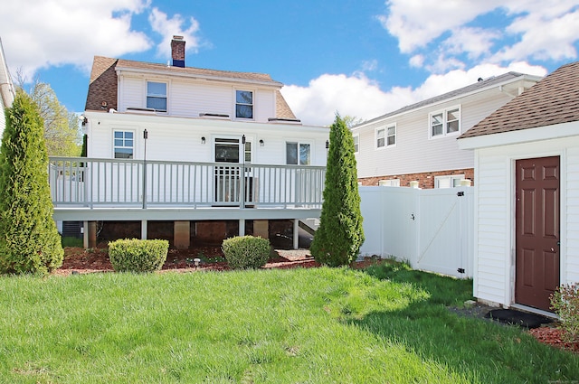 back of property featuring a chimney, roof with shingles, a lawn, a deck, and a gate