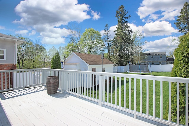 wooden terrace featuring a lawn, fence, an outbuilding, and a trampoline