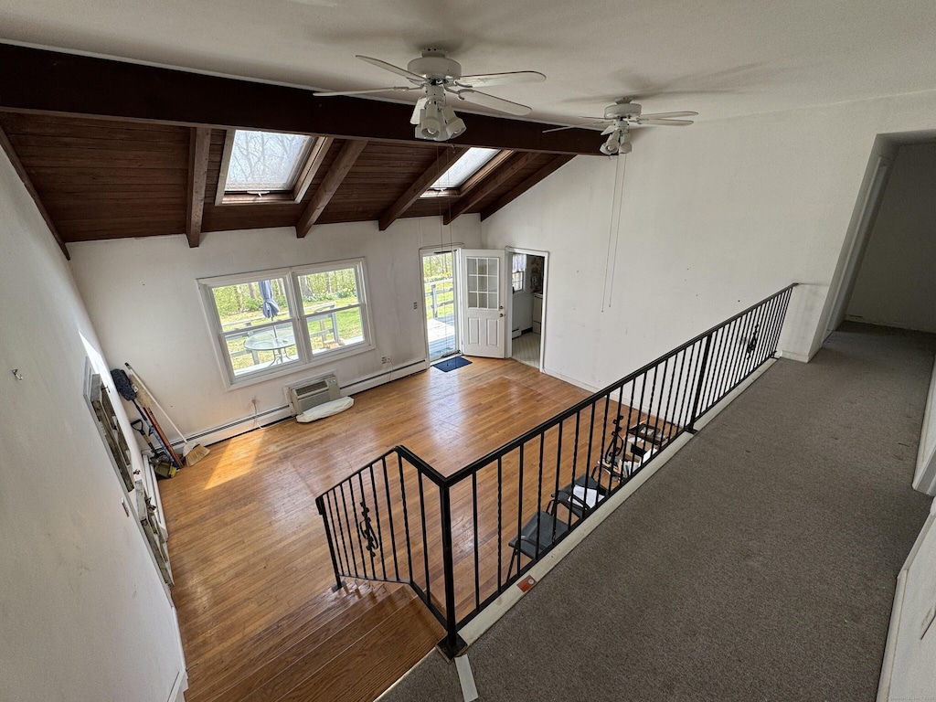 staircase with baseboard heating, ceiling fan, vaulted ceiling with skylight, and wood finished floors