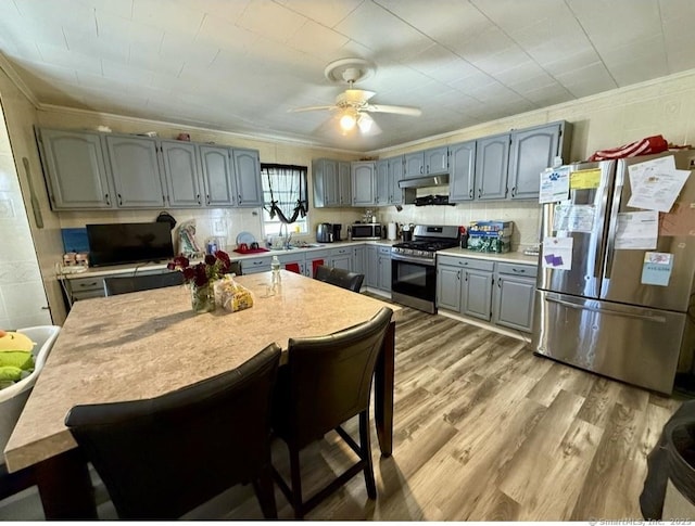 kitchen with appliances with stainless steel finishes, gray cabinets, ornamental molding, and light wood-type flooring