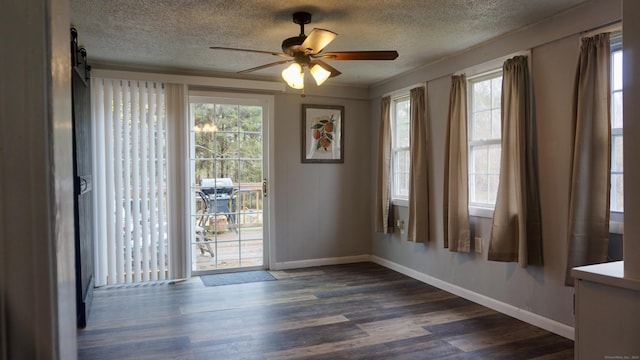 unfurnished dining area with dark wood-type flooring, a textured ceiling, a ceiling fan, and baseboards