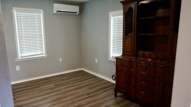 unfurnished bedroom featuring baseboards, an AC wall unit, and dark wood finished floors