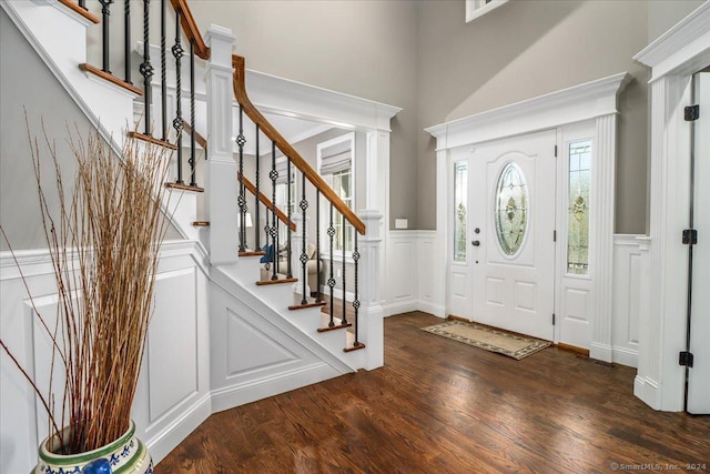 foyer entrance with a high ceiling, wood finished floors, a decorative wall, wainscoting, and stairs