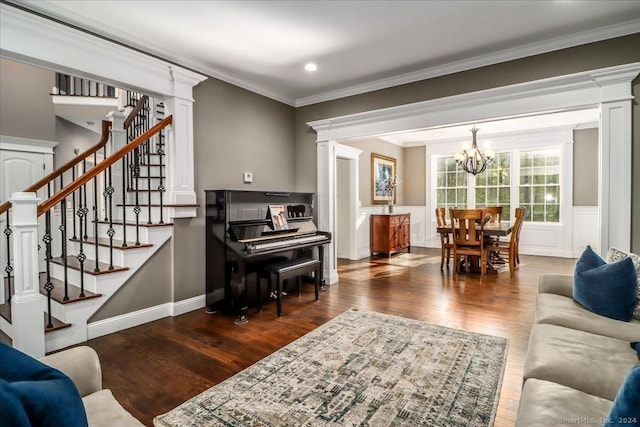 living area with a chandelier, ornate columns, wood finished floors, stairs, and crown molding
