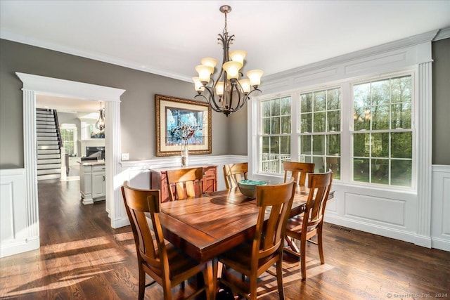 dining room with dark wood-style floors, ornamental molding, a decorative wall, wainscoting, and a chandelier