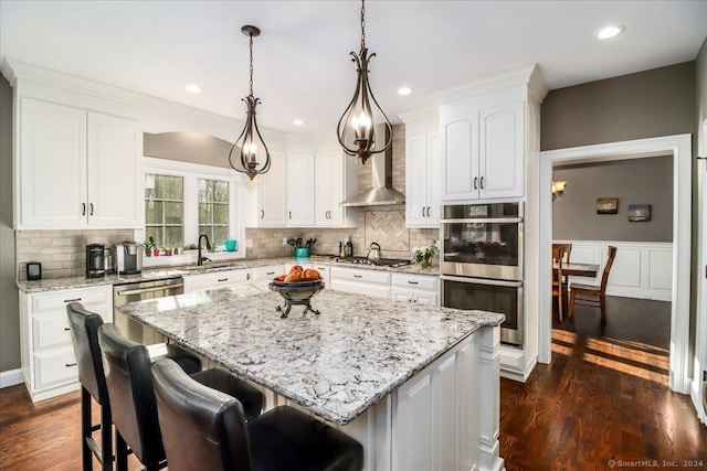 kitchen with wall chimney range hood, a sink, stainless steel appliances, white cabinets, and a kitchen island
