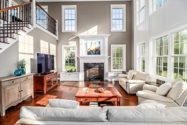 living room featuring dark wood-type flooring, a glass covered fireplace, stairway, and a high ceiling