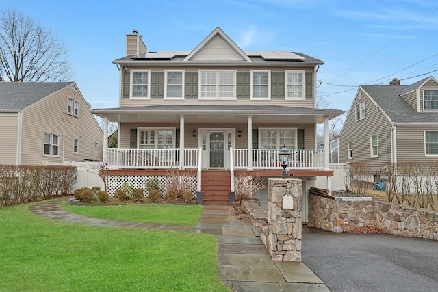 colonial-style house with a chimney, fence, solar panels, a front yard, and a porch