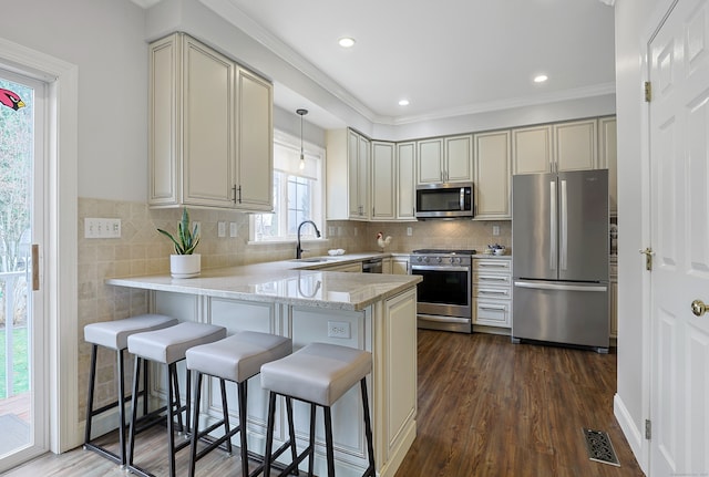 kitchen featuring a peninsula, a kitchen bar, a sink, visible vents, and appliances with stainless steel finishes