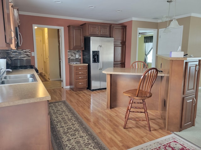 kitchen featuring stainless steel appliances, a sink, light wood-style floors, a kitchen bar, and decorative backsplash