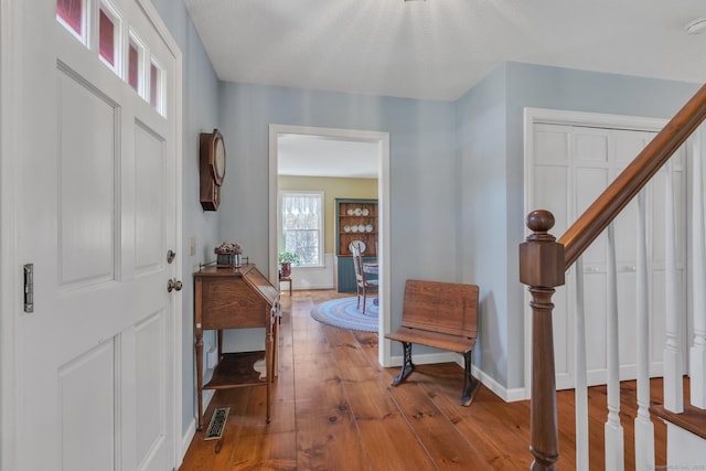 foyer featuring baseboards, hardwood / wood-style floors, visible vents, and stairs