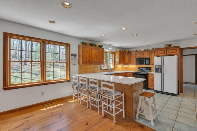 kitchen with brown cabinets, light countertops, a sink, black appliances, and a peninsula