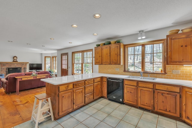 kitchen featuring dishwasher, a peninsula, a sink, and light countertops