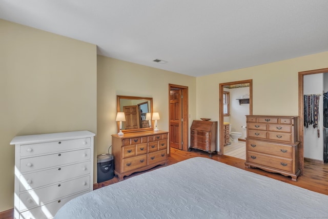 bedroom featuring ensuite bath, wood finished floors, visible vents, and a walk in closet