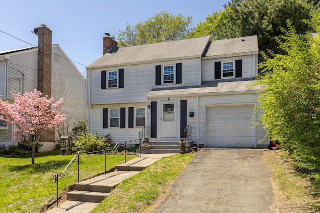 view of front of house with a front yard, an attached garage, entry steps, and aphalt driveway