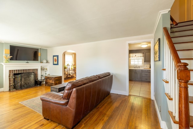 living area featuring stairs, arched walkways, crown molding, and light wood finished floors