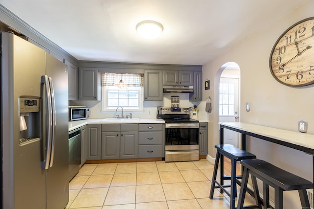 kitchen featuring a sink, arched walkways, stainless steel appliances, under cabinet range hood, and gray cabinetry