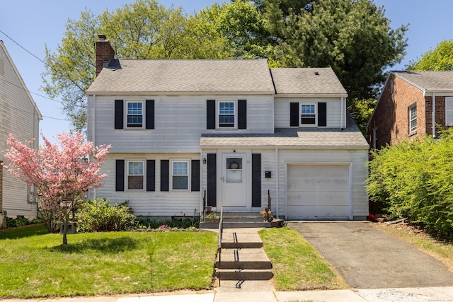 view of front facade with driveway, a chimney, a front yard, an attached garage, and a shingled roof