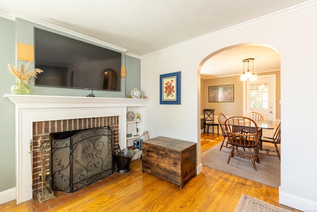 living area with crown molding, arched walkways, a brick fireplace, and wood finished floors