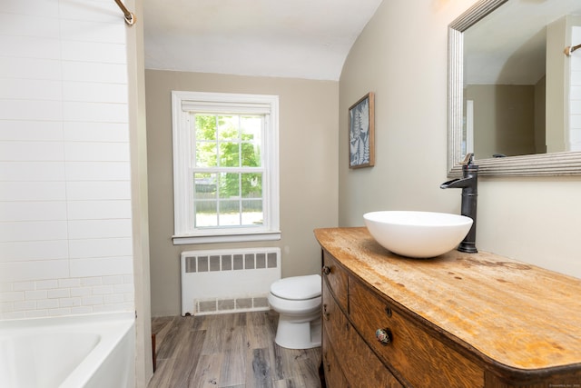 bathroom with vanity, toilet, radiator, wood finished floors, and lofted ceiling