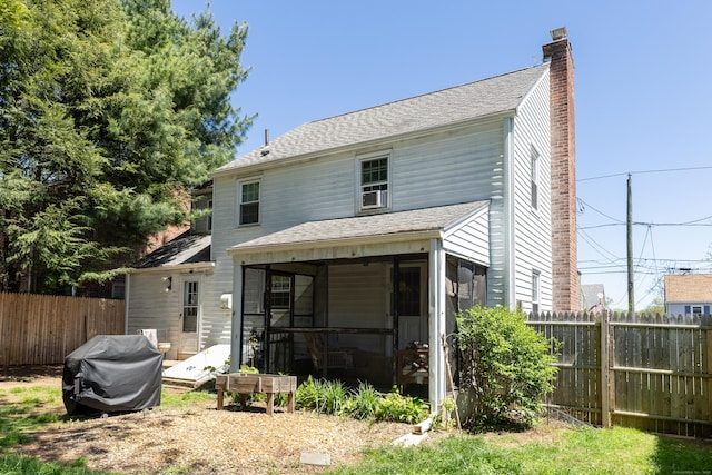 back of house with fence, a chimney, a shingled roof, and a sunroom