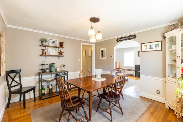 dining area with crown molding, arched walkways, baseboards, radiator heating unit, and light wood-style flooring