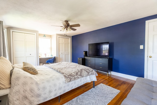bedroom featuring ceiling fan, baseboards, multiple closets, and dark wood finished floors
