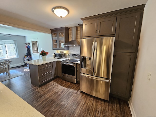 kitchen with light countertops, stainless steel appliances, wall chimney exhaust hood, a peninsula, and dark wood-style flooring