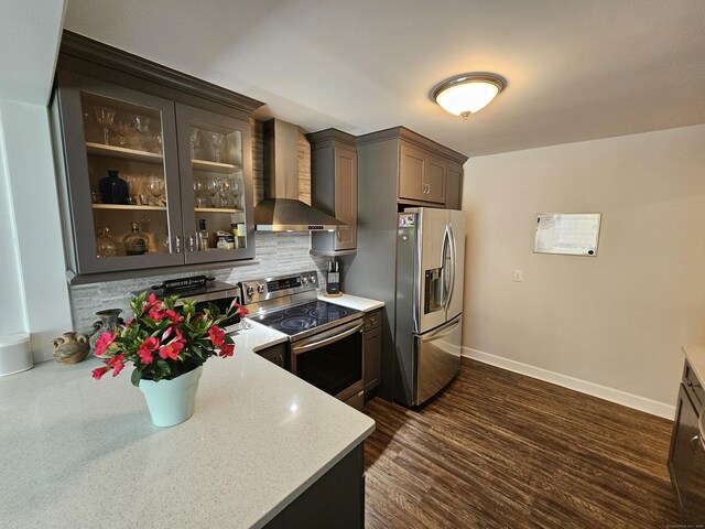 kitchen featuring stainless steel appliances, baseboards, decorative backsplash, glass insert cabinets, and wall chimney range hood