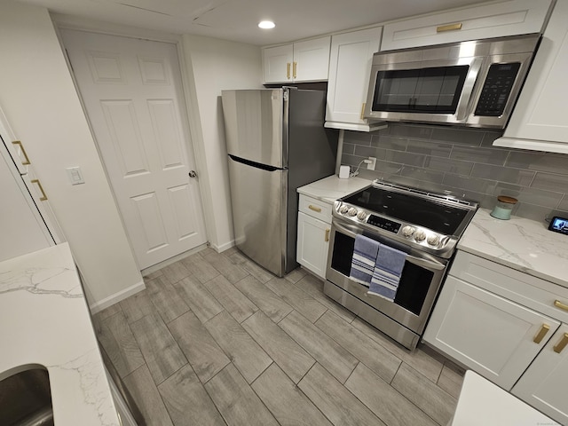 kitchen featuring light stone counters, wood tiled floor, decorative backsplash, white cabinetry, and appliances with stainless steel finishes