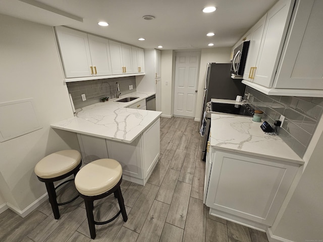 kitchen featuring light stone countertops, light wood finished floors, stainless steel appliances, and a sink