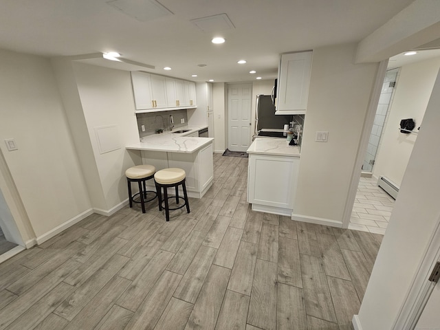 kitchen featuring white cabinets, a breakfast bar, a sink, a baseboard heating unit, and light wood-style floors