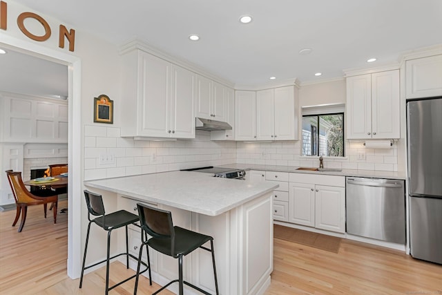 2 Donald Dr, Westport, CT 06880 - kitchen with stainless steel appliances, a sink, white cabinets, a breakfast bar, and under cabinet range hood