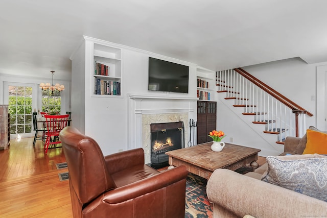 living area with hardwood / wood-style flooring, built in shelves, stairway, an inviting chandelier, and a premium fireplace