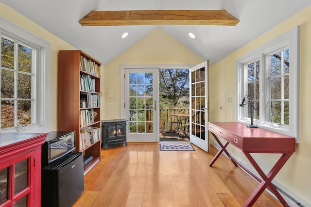 doorway to outside featuring light wood-style floors, vaulted ceiling with beams, a wood stove, and a healthy amount of sunlight