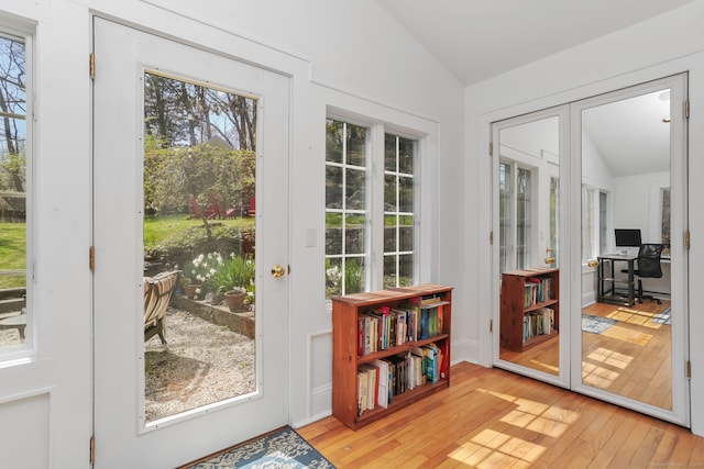 doorway with light wood-style floors, vaulted ceiling, and a wealth of natural light